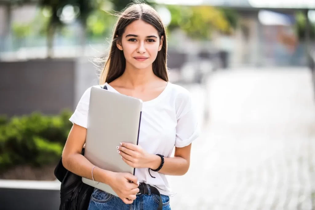 Young female student holding a laptop outdoors, ready to enroll in top German language courses in Kochi